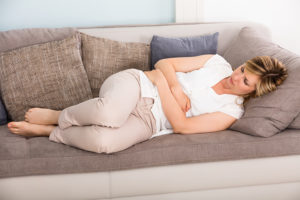 Sick woman lying on sofa and clutching her stomach