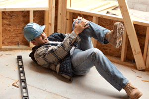 Construction worker in hard hat holding his knee after a fall on a job site