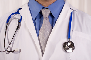 Medical provider wearing white coat, blue shirt, and gray tie with stethoscope around his neck