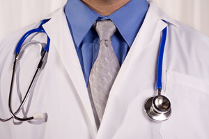 Doctor wearing a blue shirt, gray tie, and white coat with a stethoscope around his neck