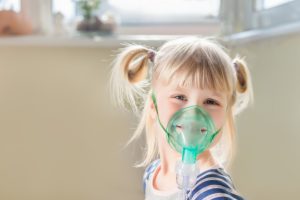 Smiling young girl with blonde pigtails receiving nebulizer treatment