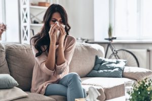 Woman sick at home sitting on couch and blowing her nose