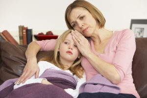 Mother cuddling her sick daughter and touching her forehead to check for fever