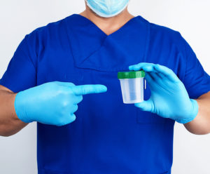 Medical professional in blue uniform holding empty container for urine sample