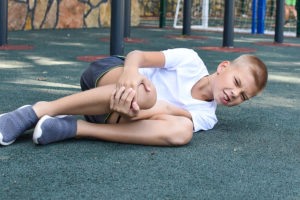 Injured child on a playground holding his painful knee