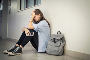 Stressed out female college student sitting on floor next to backpack