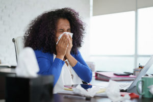 Female college student blowing her nose while studying with laptop