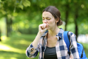 Female college student coughing while walking on campus with a backpack