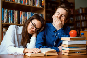 Tired college students surrounded by textbooks during an all-night study session