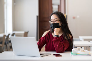 Female college student wearing a mask to help prevent norovirus while working on her laptop on campus